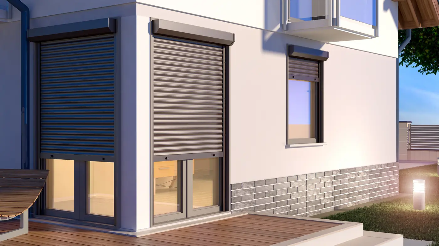 Modern home with dark aluminium roll shutters lowered over its patio doors and windows at dusk